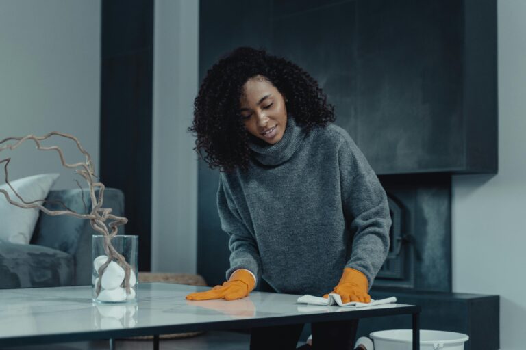 Home African American woman cleaning a table with orange gloves in a cozy, modern living room setting.